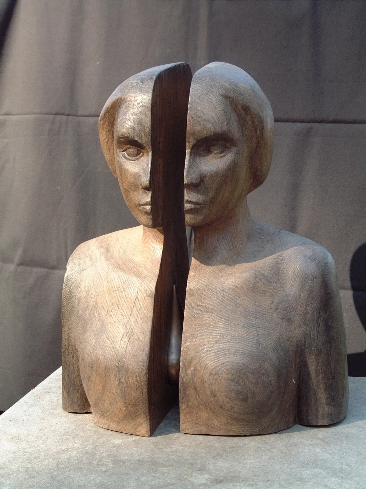 Nadzieja: busto femminile di rovere nero diviso verticalmente in due metà scostate, ciascuna con un volto; nel varco una goccia scura, appuntita in alto e gonfia all’altezza del petto