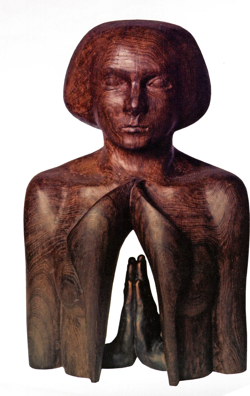 Skupienie: busto di rovere scuro lucidato, capelli a caschetto e occhi chiusi; il petto si apre in due lembi e dentro, in basso, due mani di bronzo giunte in preghiera