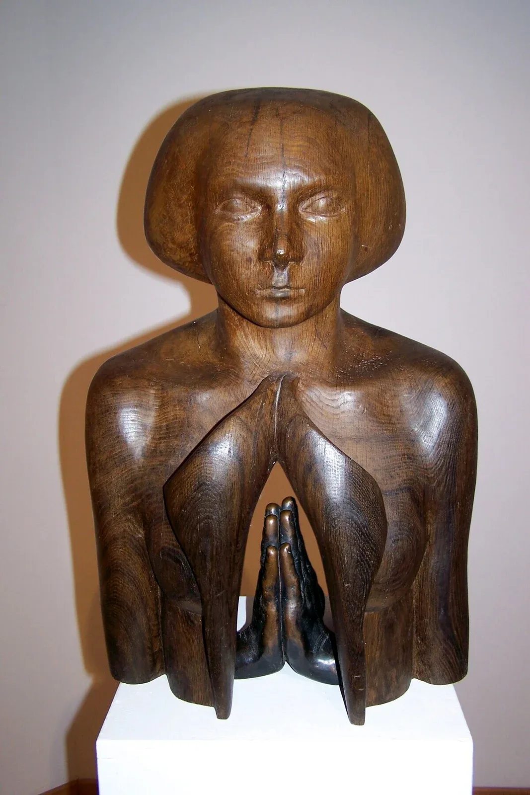 Skupienie: busto di rovere scuro lucidato, capelli a caschetto e occhi chiusi; il petto si apre in due lembi e dentro, in basso, due mani di bronzo giunte in preghiera