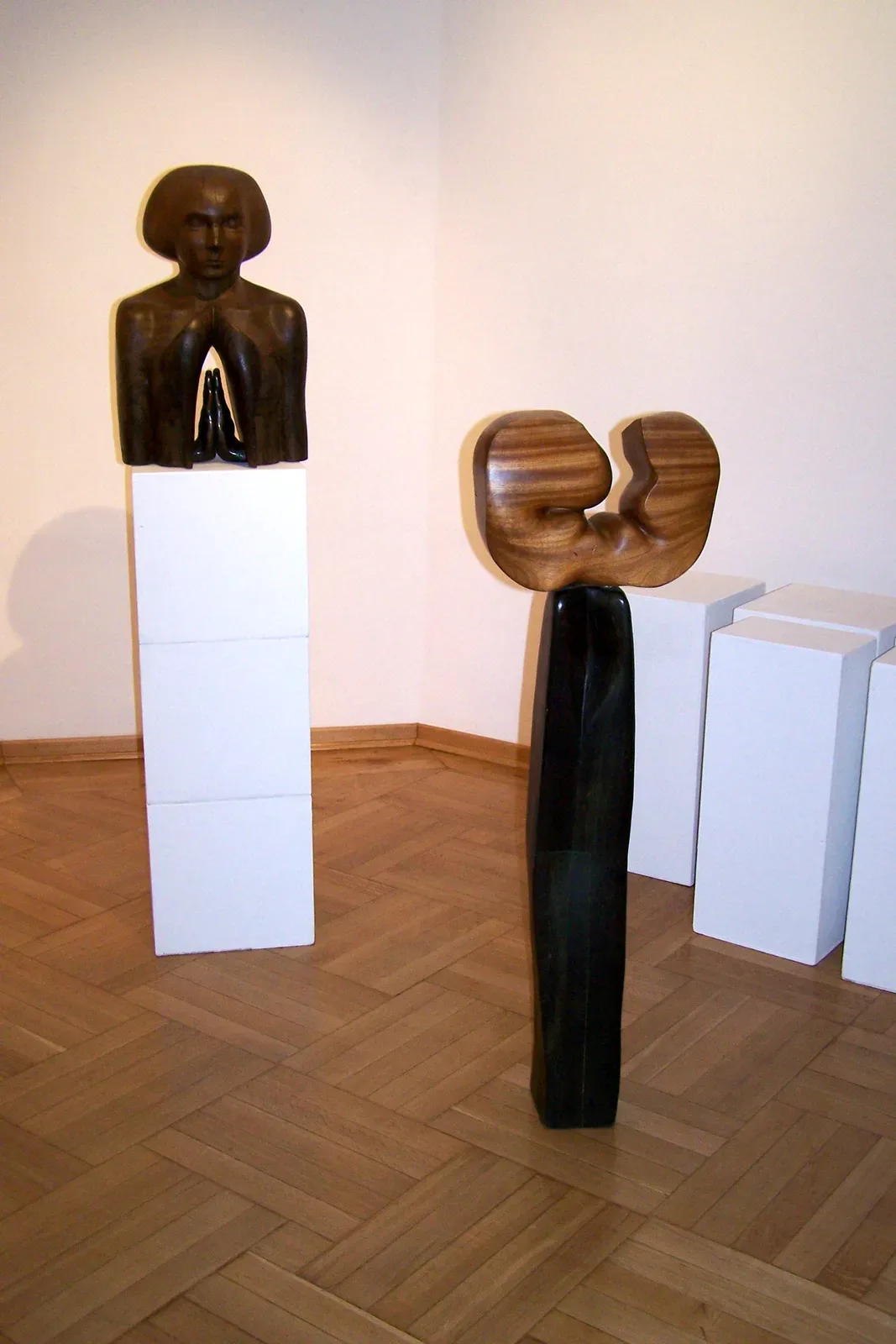Il busto di Skupienie in mostra, su un plinto bianco alto, in una sala dal parquet a spina; accanto, un’altra scultura di legno chiaro su una base scura