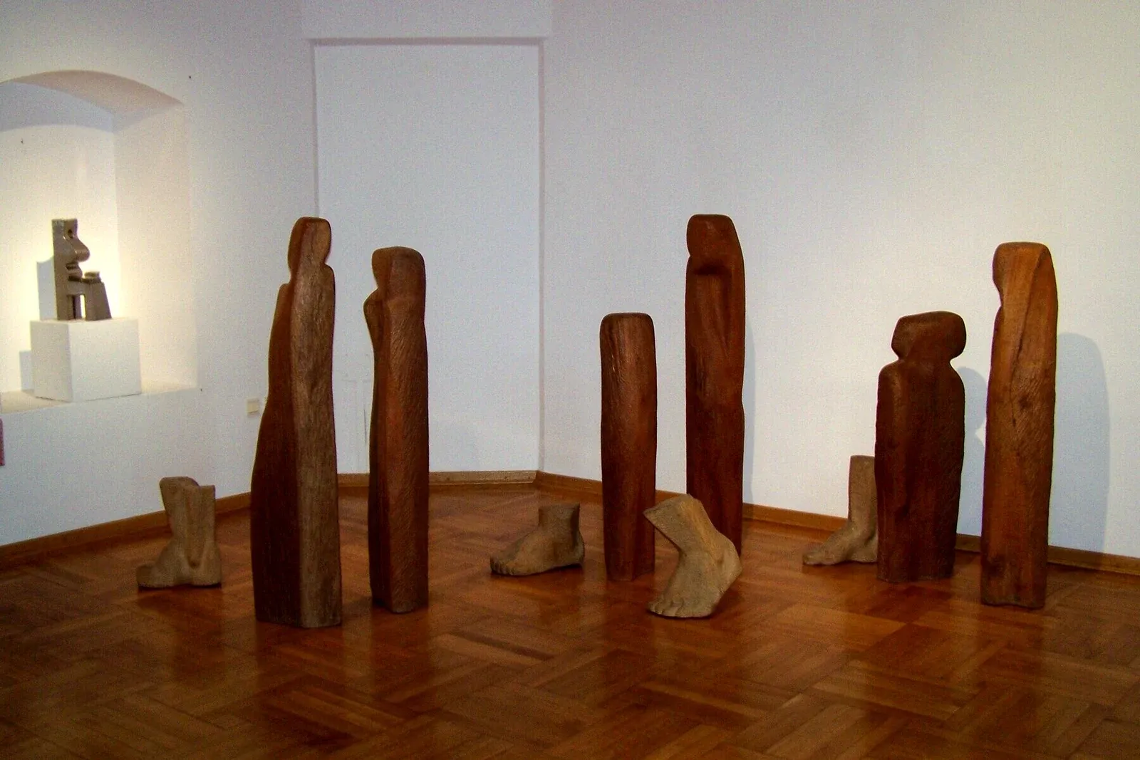 Le figure di mogano di Wygnanie disposte nell’angolo di una sala di museo, coi grandi piedi di legno sparsi sul parquet fra loro
