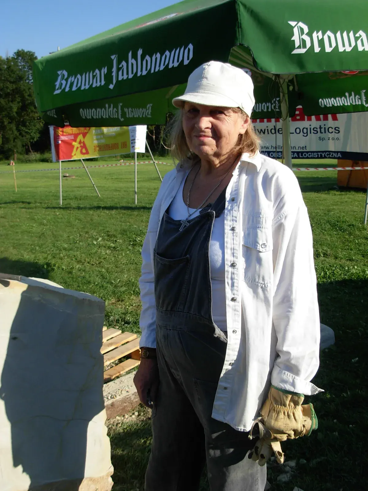Etiuda — Antonina al plein air, in tuta da lavoro e guanti in mano, accanto al blocco; alle sue spalle lo striscione «ART KONFRONTACJE — PLENER RZEŹBIARSKI — SZTUKA W PRZESTRZENI PUBLICZNEJ».