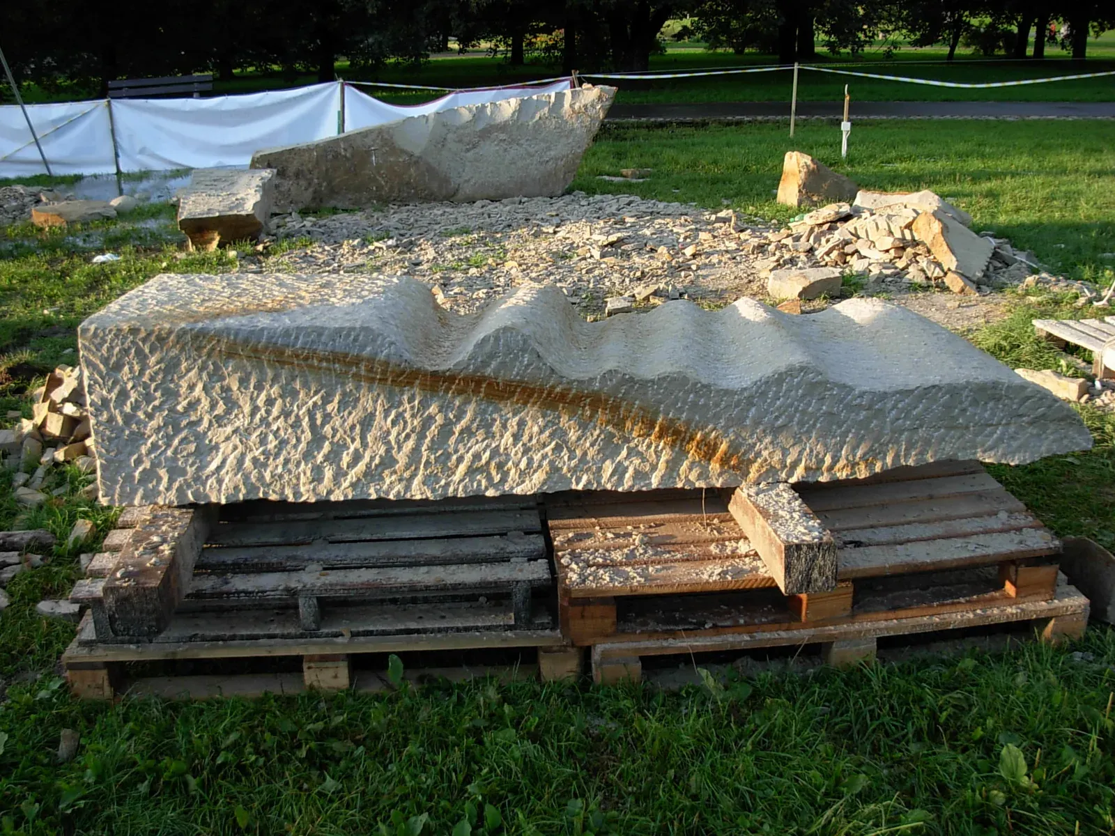 Due blocchi di arenaria accostati uno sopra l’altro sui pallet, coi profili ondulati affacciati, in mezzo al prato del parco