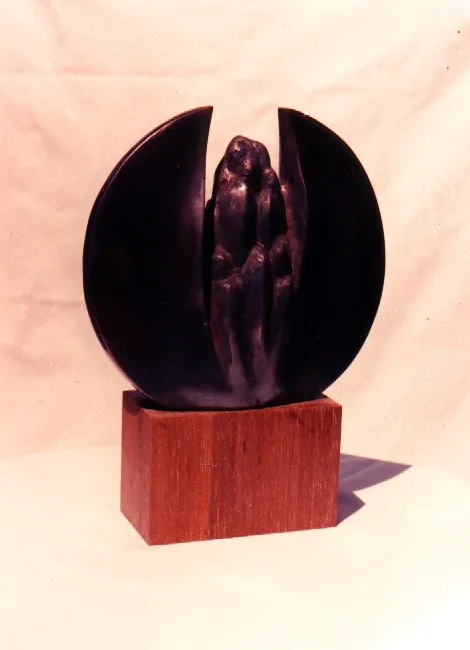 Pączkowanie: disco di bronzo diviso da una fenditura verticale in cui si addensa un grappolo di figure, su base di legno