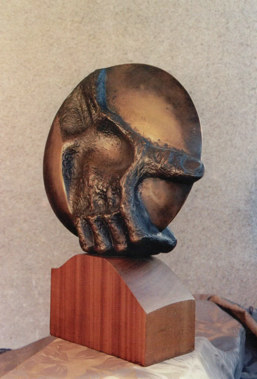 Dyskobol: disco di bronzo dalla patina calda, in piedi su una base di mogano sagomata; sulla faccia del disco una mano in rilievo lo afferra dal basso, con le dita raccolte sul bordo