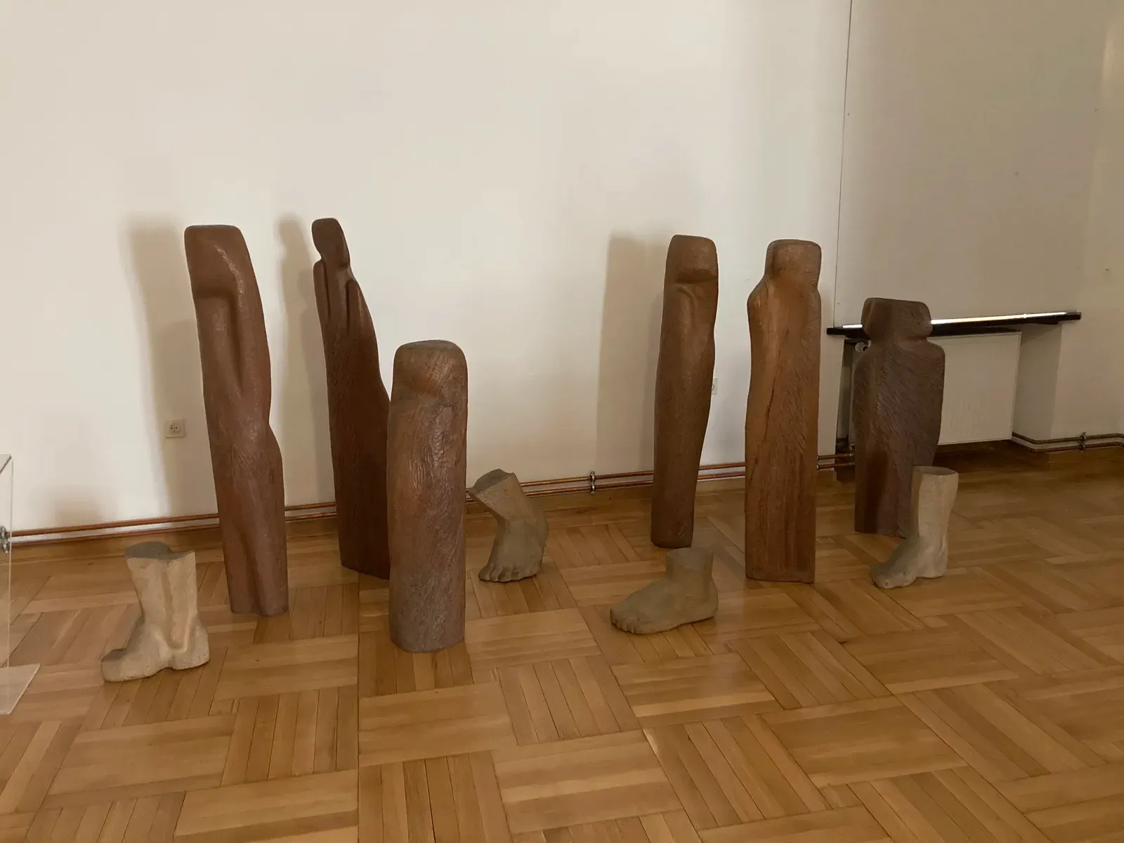 Le figure lignee di Wygnanie disposte in sala su un basamento chiaro, coi piedi scolpiti fra le figure