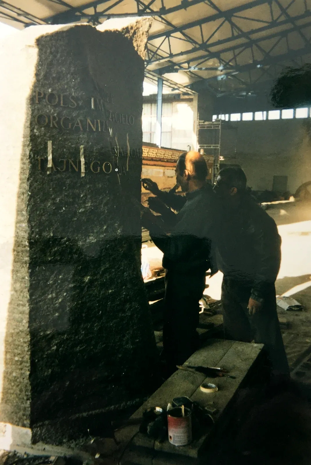 Due artigiani dorano le lettere incise sulla stele di granito scuro, in piedi nell’officina
